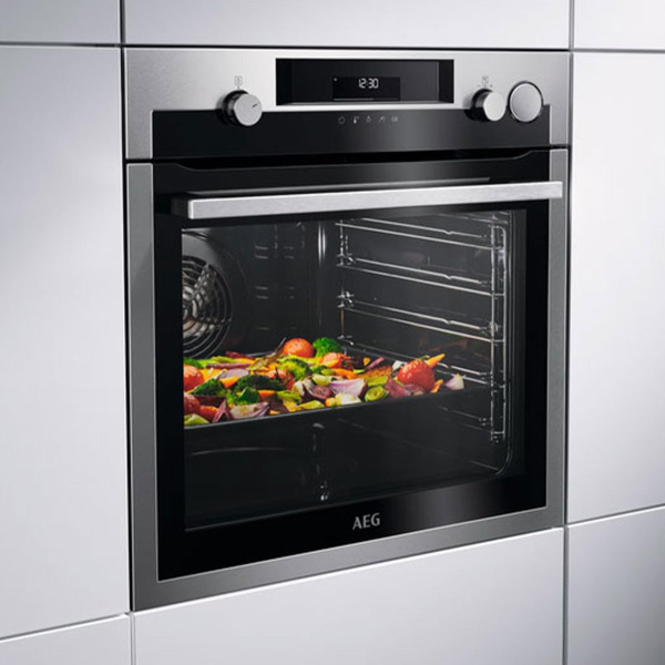 Vstavaná rúra AEG BSS578271M v kuchyni počas pečenia zeleniny, predný pohľad s displejom a dvoma ovládačmi.