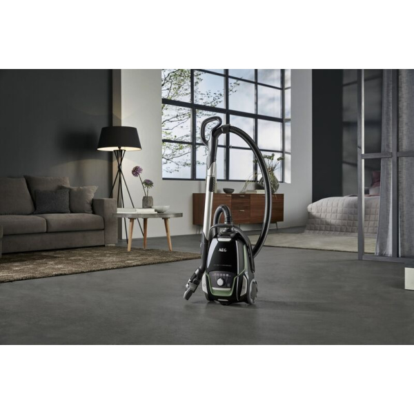 AEG VX9-2-ÖKO pri pohovke v modernej obývačke, pripojená teleskopická rúra a hadica